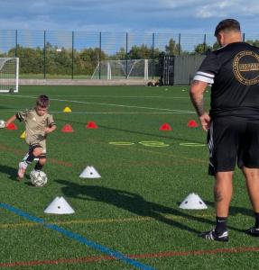 2 A Nexgen coach running a one-to-one session with a young player on an outdoor pitch