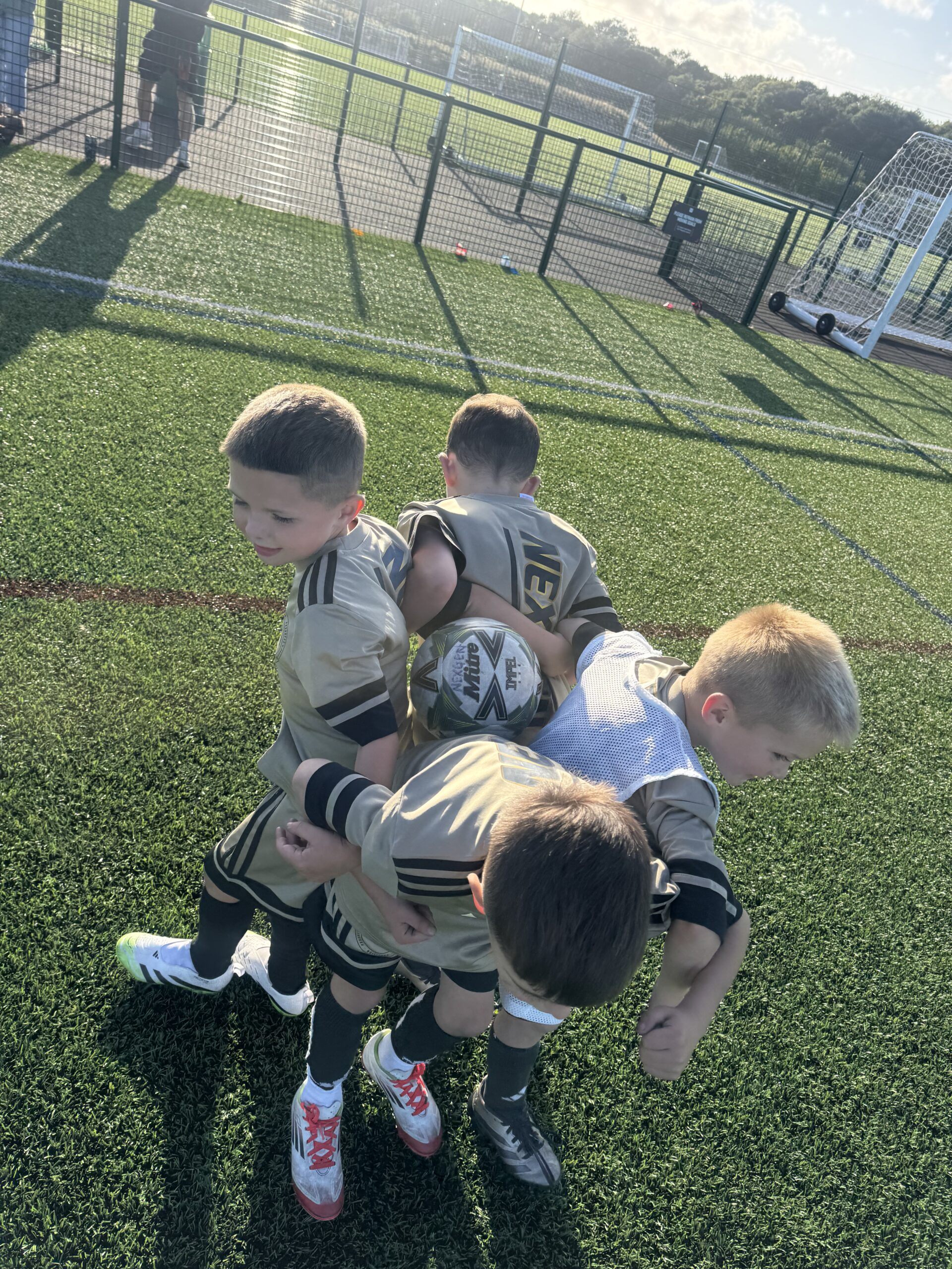 Young players in Nexgen kit gathered around the ball during a session on an outdoor pitch