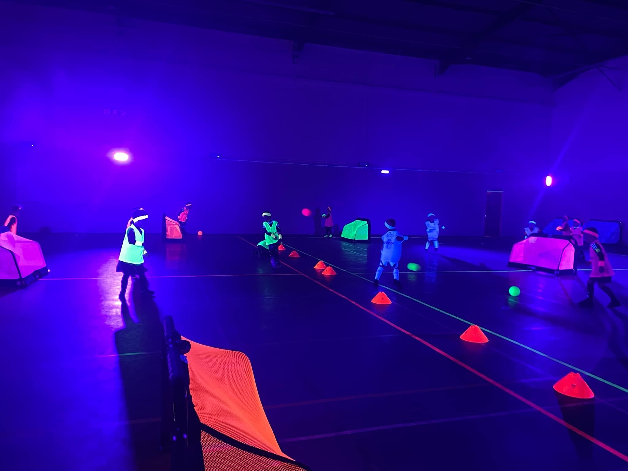 Glow-in-the-dark UV football party in a sports hall lit with blue light